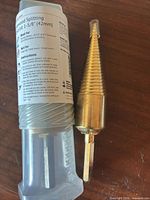 Drill bit beside clear plastic storage tube and label.