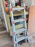 Full view of folded aluminum multi-position articulating ladder leaning against cabinet
