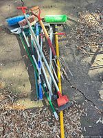 Group of assorted poles, brooms, fork, scraper on ground