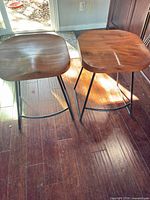 Front view of both stools showing wood seats and metal legs