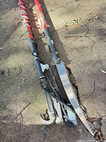 Two red telescoping pole pruners with blades and lopper heads laid on pavement