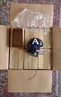 Open shipping box showing twelve individual boxed mini helmet radios and one unboxed sample