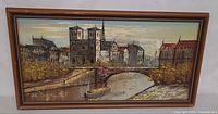 front view of framed oil painting depicting cityscape with river, bridge and boat