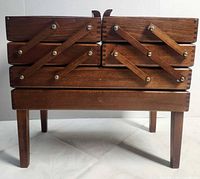 Front view of closed wooden accordion sewing box on legs showing hardware and finish