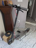 Full view of Xiaomi Mi M365 scooter with charger plugged in, honeycomb tires and box visible