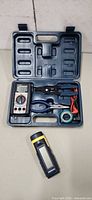 Open plastic case showing multimeter, pliers, wire stripper, leads, tape and separate moisture tester
