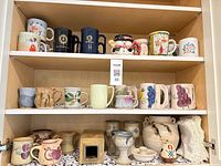 Cabinet view showing full assortment of mugs, goblets, pitchers, planters, jar and vase