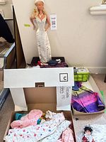 Barbie doll standing on base with boxes of assorted clothes and souvenir doll visible