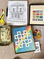 Group shot of all items—two framed stamp sheets, architectural print, tray of loose stamps, ribbon magnet and wooden magnet