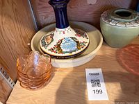 Shelf view showing commemorative ceramic decanter, stack of four pink glass bowls, and partial view of green vase
