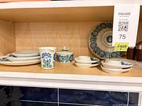 Dinnerware pieces on shelf: stack of dinner plates, creamer, sugar bowl, side plates, salt & pepper