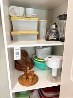 Cabinet shelf showing plastic containers, Oster blender base and pitcher, water filter pitcher, wooden bowls and boards