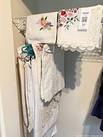 Folded tablecloths, runner and embroidered napkins hanging on wire shelf