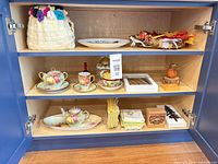 Cabinet showing full assortment: crocheted tote, plate, leaf arrangement, tea set pieces, jars, linens and decor