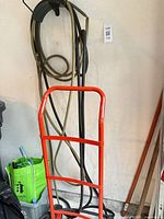 Overall view of red Sears hand truck with two coiled garden hoses hanging behind