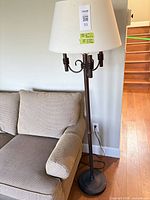 Full view of lamp next to sofa showing height, shade, decorative arms and finish