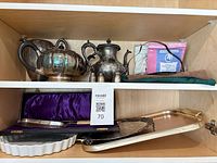 Complete lot on cupboard shelves showing tea service, shakers, porcelain trays, cake server case and polishing cloths