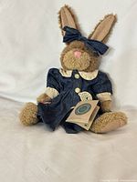 Front view of tan plush bunny in denim dress, bow on ear, tags attached