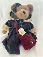 Full view of teddy bear dressed in plaid coat, hood, bow, and red bag