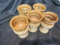 Five brown stoneware pedestal mugs on dark fabric