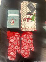 Folded aqua Santa towel, folded beige snowman towel, two red snowflake oven mitts