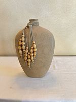 Front view of beige clay vase with wooden bead tassel accent