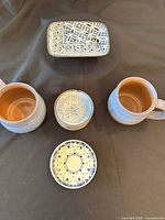 Assorted pieces laid out: one tray, two mugs, stack of bowls, floral plate