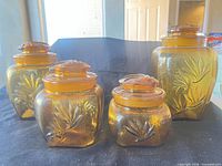 Group shot displaying all four amber glass jars with lids showing size variation and embossed leaf motif
