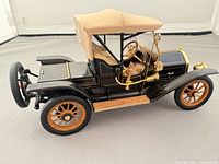 Left side view of the die-cast 1910 Cadillac showing tan roof, black body, brass trim, wood wheels