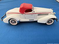 Full side view of white 1935 Auburn model with red top on blue backdrop