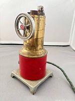 Full view of brass vertical boiler engine on red base with green cord