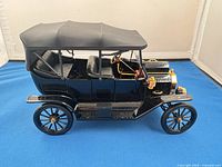 Left side view of black Ford Model T scale model showing fabric top, gold/brass trim, wheels, and interior