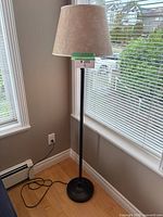 Full view of floor lamp in corner showing base, pole, shade and cord
