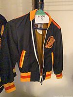 Front view of black Canucks bomber jacket on hanger displaying logo and zipper