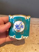 Front view of teal porcelain toothpick holder with floral medallion and gold trim