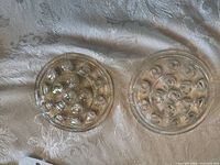 Two circular clear glass flower frogs on fabric surface