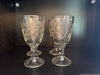 Four clear embossed glass goblets on shelf