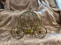 Front view of gold metal pumpkin carriage showing scroll wheels and tealight holder