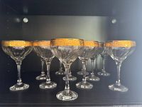 Front view of 11 gold-rimmed champagne coupes on shelf