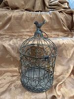Full view of metal birdcage front, showing scroll design and bird finial