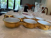 Side view of six bowls showing gold exterior, white interior, handles