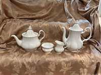 Full set showing coffee pot, teapot, creamer and sugar bowl on fabric backdrop