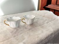 Two white Shelley bone china teacups with scalloped rims and gold handles on surface