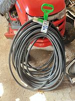Full view of coiled 100' black garden hose with green carry handle
