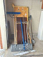 Group of garden tools and wood pieces leaning against garage wall