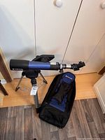 Meade blue refractor telescope on tripod beside soft case