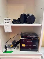 Camera, strap, cables and box displayed on shelf