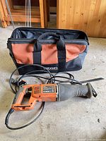 Ridgid R3001 reciprocating saw with power cord and fitted blade in front of tool bag