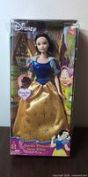 Front view of boxed Snow White doll showing figure, dress, and accessory