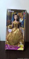 Front view of boxed Belle doll with gold gown and ring accessory visible